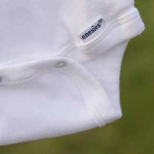 Op de afbeelding: Witte romper met een drukknoop sluiting en het woord "onesies" gedrukt op de voorkant.