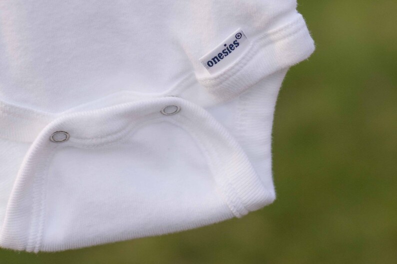 Op de afbeelding: Witte romper met een drukknoop sluiting en het woord "onesies" gedrukt op de voorkant.