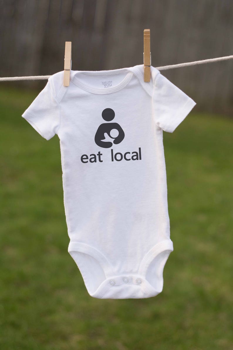 Op de afbeelding: Een witte baby romper met een zwarte afbeelding van een persoon die een baby vasthoudt en de tekst "eat local".