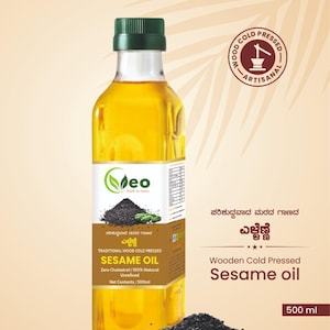 May include: A clear glass bottle of sesame oil with a green label that reads "Vasantha Eco & Organics" and "Traditional Wood Cold Pressed Sesame Oil". The bottle is sitting on a wooden surface with black sesame seeds scattered around it. The label also states "Zero Cholesterol | 100% Natural | Unrefined" and "Net Contents: 500ml".