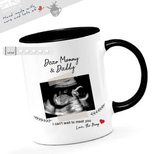 May include: A white ceramic mug with a black interior and handle. The mug features the text "Dear Mommy & Daddy" and an ultrasound image. Below the image is the text "I can't wait to meet you Love, The Bump".