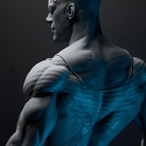 May include: A gray figurine of a superhero, viewed from the back and side. The figure has a muscular physique, with detailed textures on the suit and hair. The lighting creates shadows, highlighting the form and design.