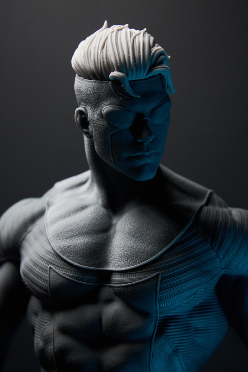 May include: A grayscale superhero figurine with a detailed physique and stylized hair. The figure has a mask-like design over the eyes and a textured costume. The lighting creates dramatic shadows, highlighting the muscular form.