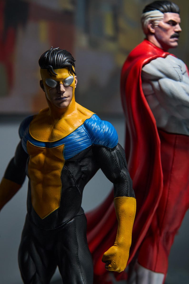 May include: Two action figures of superheroes. The first figure is in a yellow and blue suit with a black undersuit. The second figure is in a white and red suit with a red cape. The figures are highly detailed and posed in a dynamic stance.