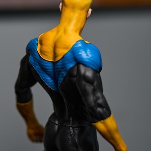 May include: A figurine of a superhero from the back, showcasing a yellow head and shoulders, blue and black suit. The figure has a muscular physique and is posed in a dynamic stance. The colors are vibrant and the details are well-defined.