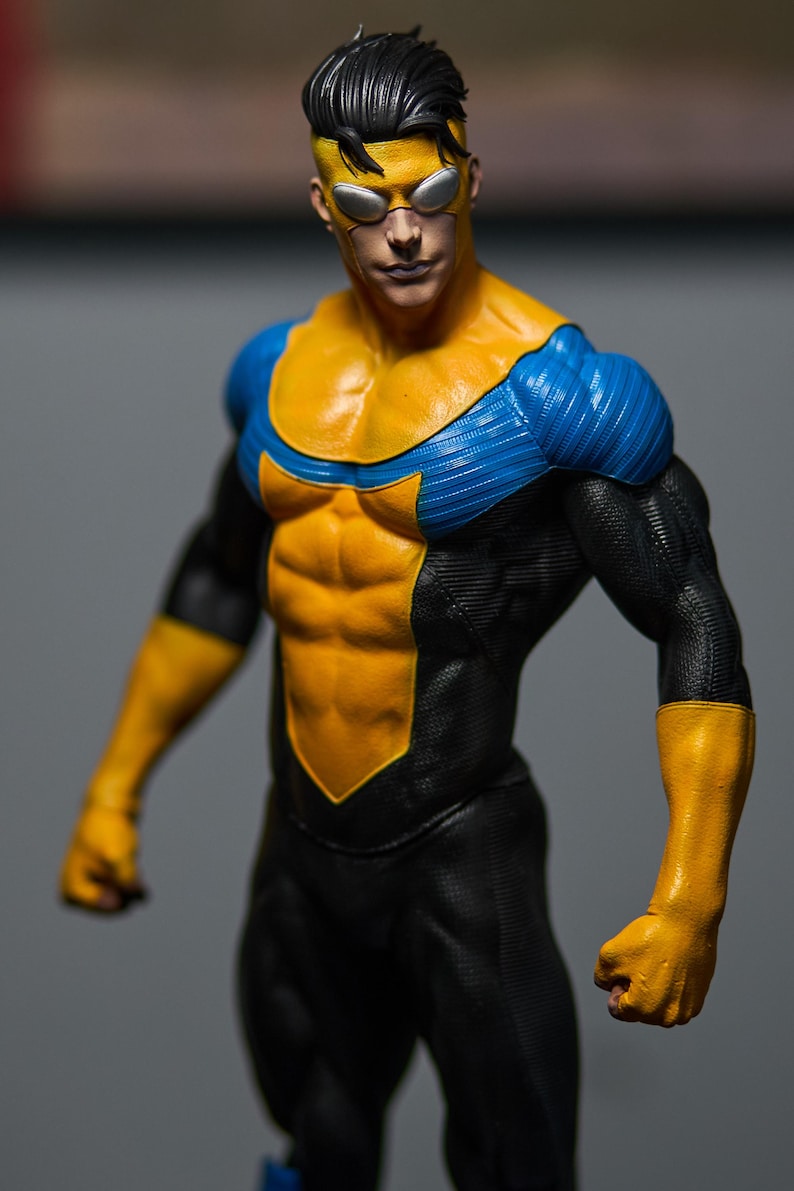 May include: A detailed action figure of a superhero in a dynamic pose. The figure is clad in a black, yellow, and blue costume. The yellow accents highlight the chest, arms, and gloves, while blue accents are on the shoulders. The figure has a determined expression.
