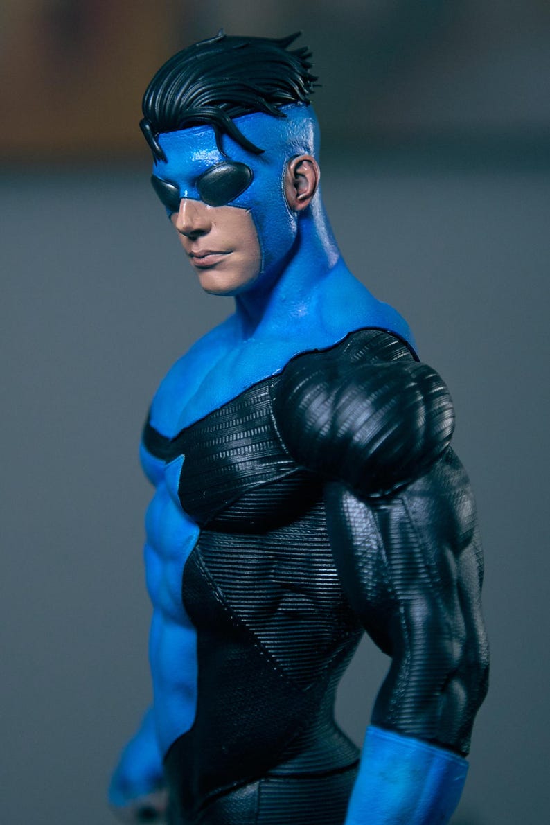 May include: A blue and black superhero action figure. The figure is wearing a blue mask, a blue and black suit with textured details, and has black hair. The figure is posed in a dynamic stance, showcasing its muscular physique.