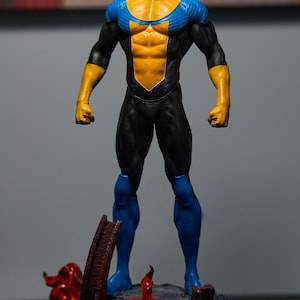 May include: A figurine of a superhero in a dynamic pose. The figure is clad in a black suit with yellow and blue accents. The base features a rocky terrain with red and orange flame details, adding a dramatic effect to the collectible.