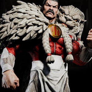 May include: A 1/6 scale collectible figure of a muscular character with a dark mustache, wearing a red textured bodysuit, a white loincloth, and a large, light-colored fur mantle featuring a lion head design with orange eyes and a gold circular emblem.