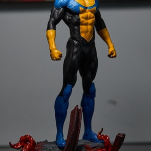 May include: A figurine of a muscular superhero in a dynamic pose. The figure is predominantly yellow and black, with blue accents on the shoulders and legs. It stands on a detailed base with red flame-like elements.