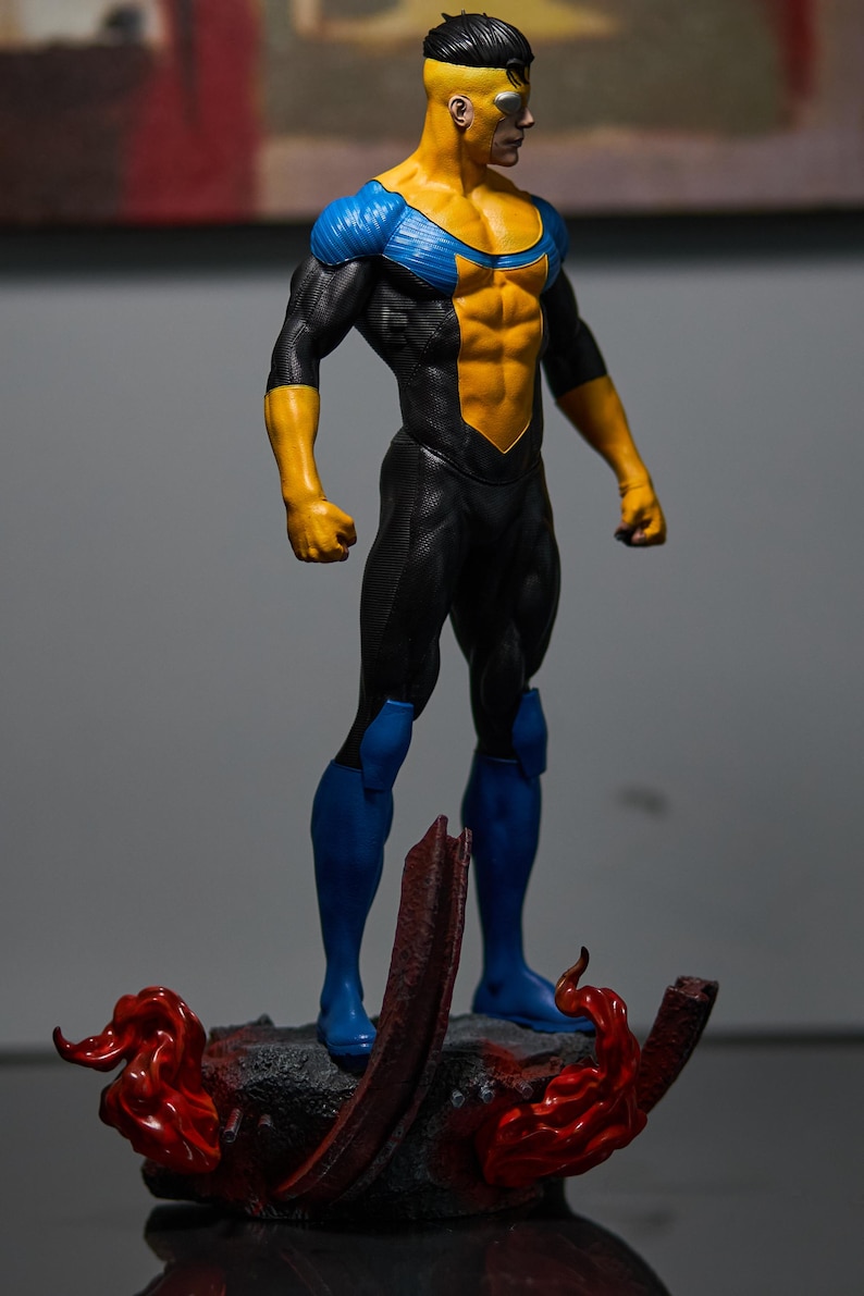 May include: A figurine of a muscular superhero in a dynamic pose. The figure is predominantly yellow and black, with blue accents on the shoulders and legs. It stands on a detailed base with red flame-like elements.