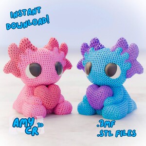 May include: Two 3D printed axolotl plushies, one pink and one blue, holding hearts in their hands. The pink axolotl has the text "AMY CR" on its base. The blue axolotl has the text ".3MF .STL FILES" on its base.