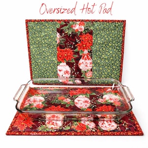 May include: An oversized hot pad with a Christmas theme. The pad is red with a floral pattern and a green border. A clear glass baking dish sits on the pad. The text "Oversized Hot Pad" is in red script.