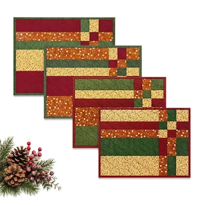 May include: Set of four rectangular quilted placemats. Each placemat features a patchwork design with alternating stripes of burgundy, green, gold, and orange fabrics. The placemats have a burgundy border and are arranged in a staggered display.