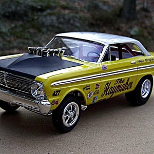 May include: A yellow and black vintage race car model with chrome accents. The car features the text "The Haymaker" and "New England Ford Dealers". The hood is black, and the roof is silver. The car has a large engine and racing tires.