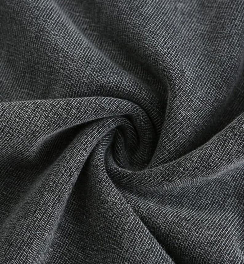 May include: Close-up of a dark grey fabric with a textured weave. The fabric is folded and draped, creating shadows and highlights that emphasise the texture and depth of the material. The weave pattern is visible throughout.
