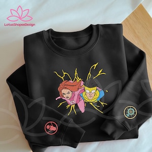 May include: Black crewneck sweatshirt featuring an embroidered design of two cartoon superheroes with yellow lightning bolts. The sweatshirt has two circular embroidered patches on the sleeves. The LotusShopeeDesign logo is visible in the top left corner.