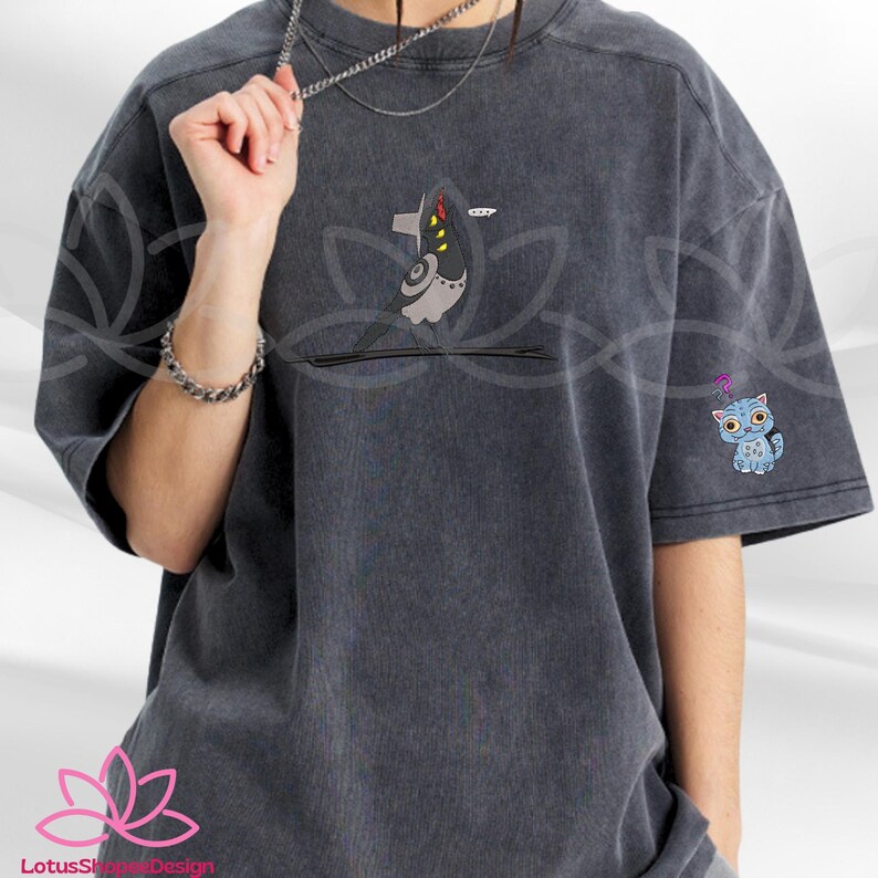 May include: Dark gray t-shirt with two embroidered designs. One design is a stylized bird with yellow accents, and the other is a blue cat with a question mark above its head. The shirt has short sleeves and a relaxed fit.