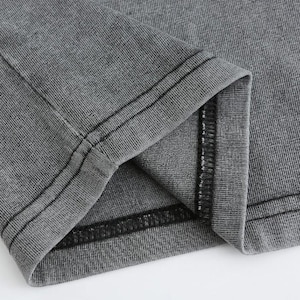 May include: Close-up of a gray fabric garment, possibly a t-shirt or shirt, with visible seams and stitching. The fabric has a textured appearance, and the seams are reinforced with black thread. The garment is folded, revealing the inside.