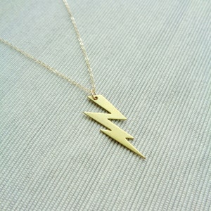 May include: A gold lightning bolt pendant necklace on a silver chain. The necklace is on a textured gray surface.