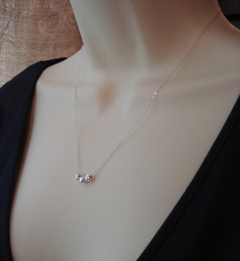May include: A silver chain necklace with three small silver beads.