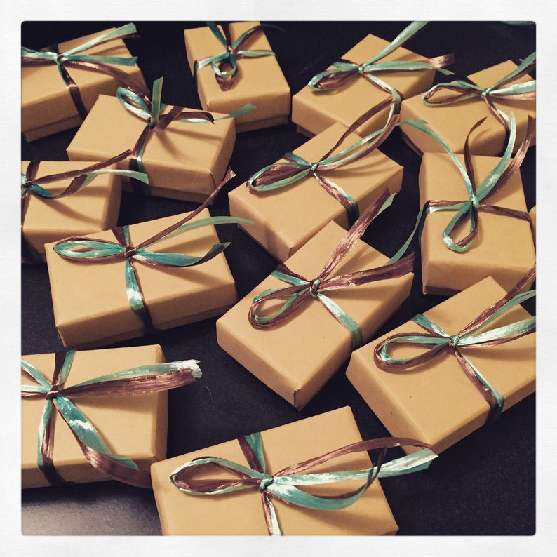 May include: A collection of small, brown cardboard boxes tied with teal and brown ribbon. The boxes are arranged in a random pattern on a black surface.