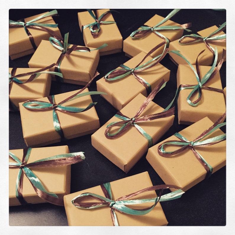 May include: A collection of small, brown cardboard boxes tied with teal and brown ribbon. The boxes are arranged in a random pattern on a black surface.