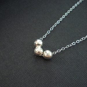 May include: A silver necklace with three faceted silver beads. The beads are connected by a silver chain.