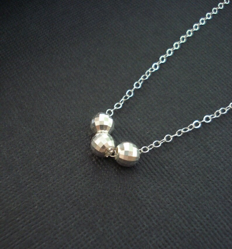 May include: A silver necklace with three faceted silver beads. The beads are connected by a silver chain.
