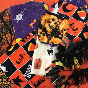 May include: Assortment of Halloween fabric scraps in orange, black, and purple with various patterns including skulls, candy corn, and a spider web.  The fabric scraps are arranged on a bright orange surface.
