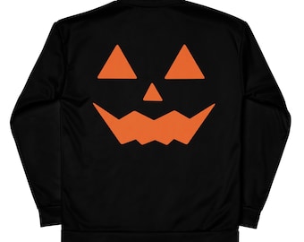 May include: Black jacket featuring a large orange jack-o'-lantern face on the back. The design includes two triangular eyes, a triangular nose, and a jagged mouth. The jacket has a full zipper and long sleeves.