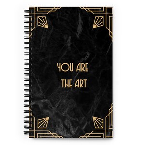May include: Black spiral notebook with a gold art deco design and the text "YOU ARE THE ART" on a black marble background.