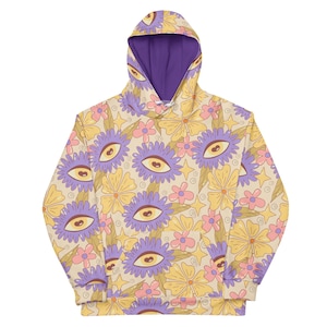 May include: A purple and yellow hoodie with a floral pattern featuring stylized eyes and flowers. The hoodie has a purple hood lining.