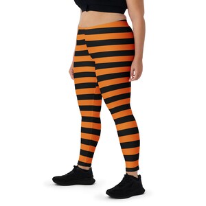 Pode incluir: Leggings compridas com riscas horizontais pretas e laranja. As leggings são justas e feitas de um material elástico. A modelo usa ténis pretos e um top preto.