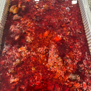 May include: A large metal pan filled with a red stew. The stew is thick and chunky, with visible pieces of vegetables and meat.