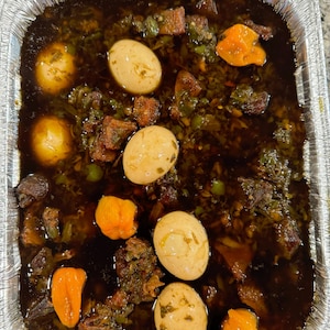 May include: A silver aluminum container filled with a dark brown stew with chunks of meat, hard-boiled eggs, and orange peppers.