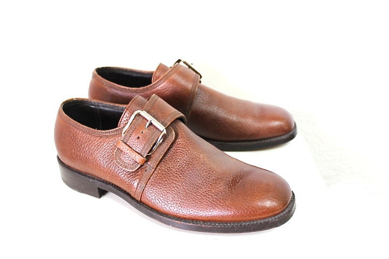 May include: A pair of brown leather monk strap shoes with a single buckle on each shoe.