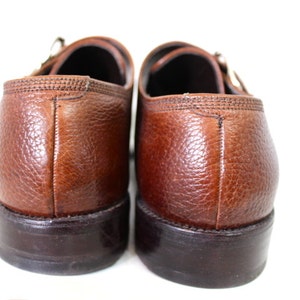 May include: A pair of brown leather monk strap shoes with a textured finish. The shoes have a dark brown sole and a buckle closure.