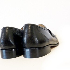 Pode incluir: Um par de sapatos de couro preto com um design cl&aacute;ssico. Os sapatos t&ecirc;m uma parte superior de couro liso e uma sola de borracha.