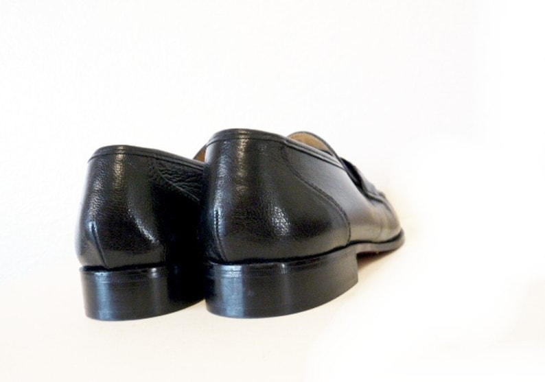 Pode incluir: Um par de sapatos de couro preto com um design cl&aacute;ssico. Os sapatos t&ecirc;m uma parte superior de couro liso e uma sola de borracha.