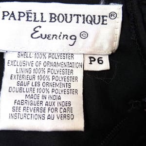 May include: Close-up of a black garment tag from Papell Boutique Evening. The tag is white with black text, including fabric composition and care instructions. A size P6 tag is attached. The garment appears to be made in India.