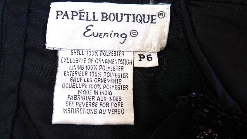 May include: Close-up of a black garment tag from Papell Boutique Evening. The tag is white with black text, including fabric composition and care instructions. A size P6 tag is attached. The garment appears to be made in India.