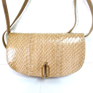 Pode incluir: Bolsa transversal bege com padrão de pele de cobra. A bolsa tem formato curvo, uma alça longa e um fecho dourado. A bolsa é feita de um material texturizado e tem um design costurado.