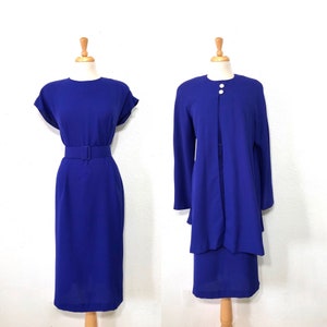 May include: A royal blue dress suit with a matching jacket and skirt. The skirt has a belt and the jacket has a single button closure.