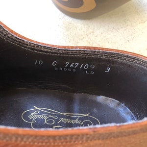May include: Close-up of the inside of a brown leather shoe with the text "10 C 767109 3 93059 LD" and the brand name "Crockett & Jones" printed on the insole.
