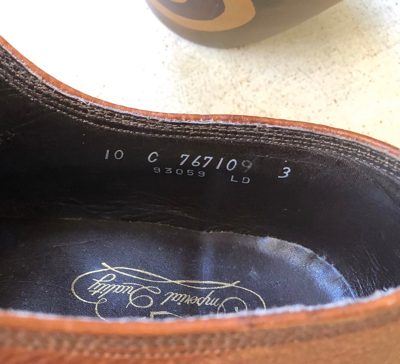 May include: Close-up of the inside of a brown leather shoe with the text "10 C 767109 3 93059 LD" and the brand name "Crockett & Jones" printed on the insole.