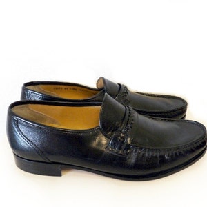 Pode incluir: Um par de sapatos de couro preto com um detalhe costurado em torno da ponta e uma &uacute;nica tira na parte superior.