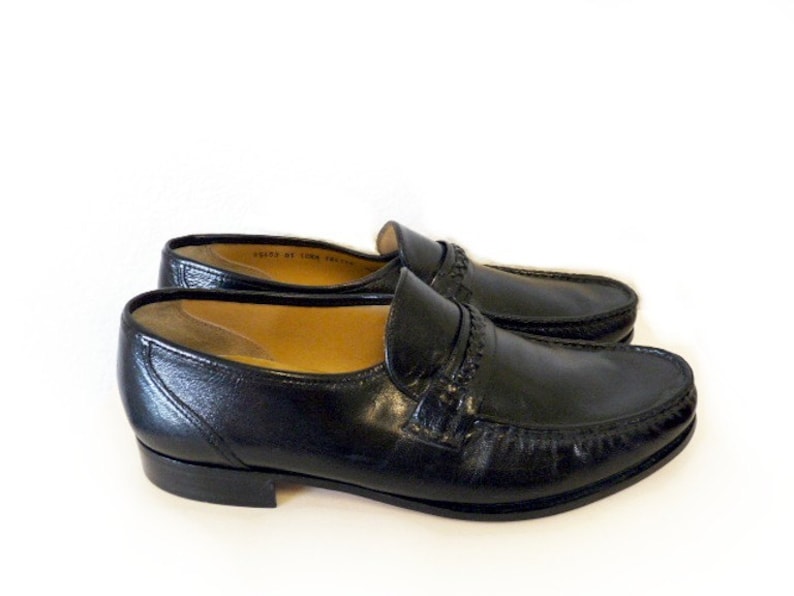 Pode incluir: Um par de sapatos de couro preto com um detalhe costurado em torno da ponta e uma &uacute;nica tira na parte superior.