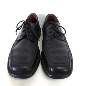 May include: A pair of black leather lace-up shoes with a rounded toe and a stitched design on the front. The shoes have a black rubber sole.