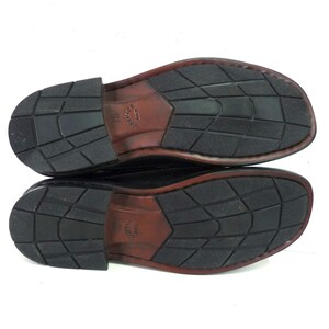 May include: The bottom of a pair of black leather shoes with a brown leather trim. The shoes have a textured rubber sole.
